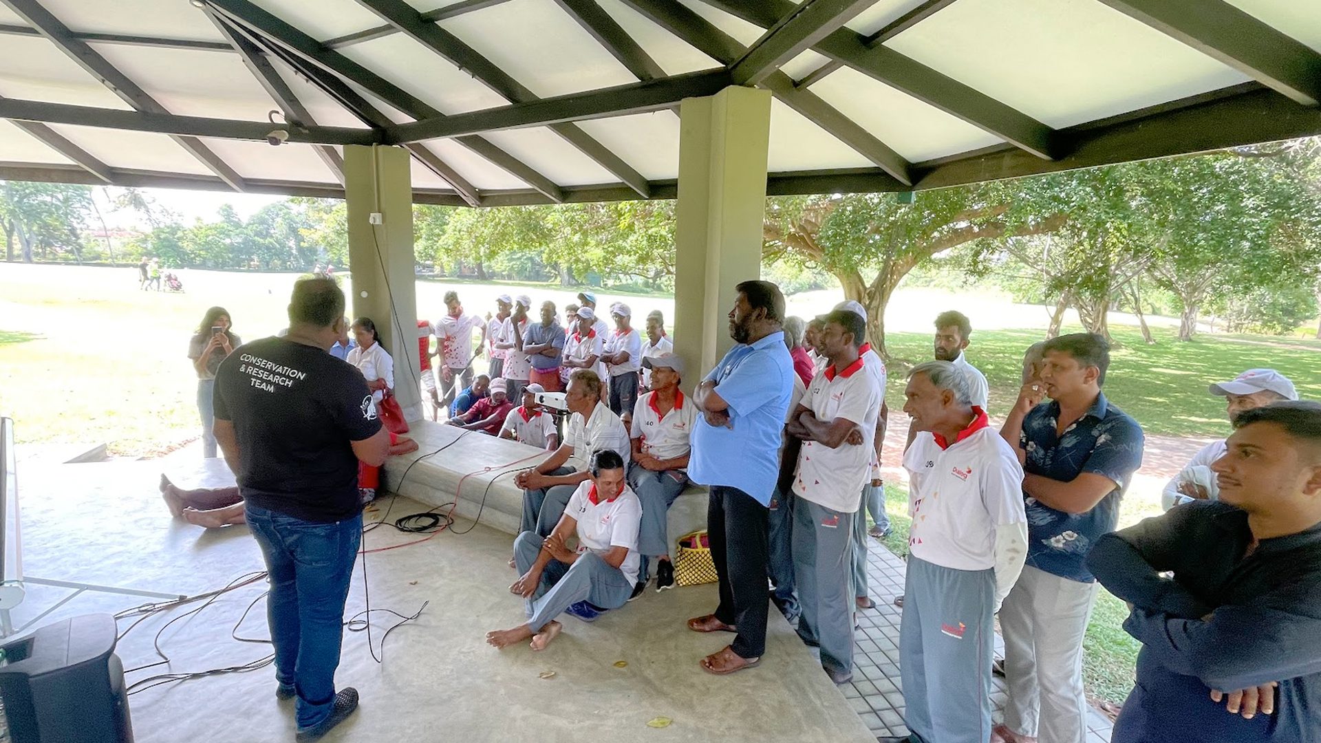 A project team member addressing a group of participants gathered under an open shelter beside a wetland