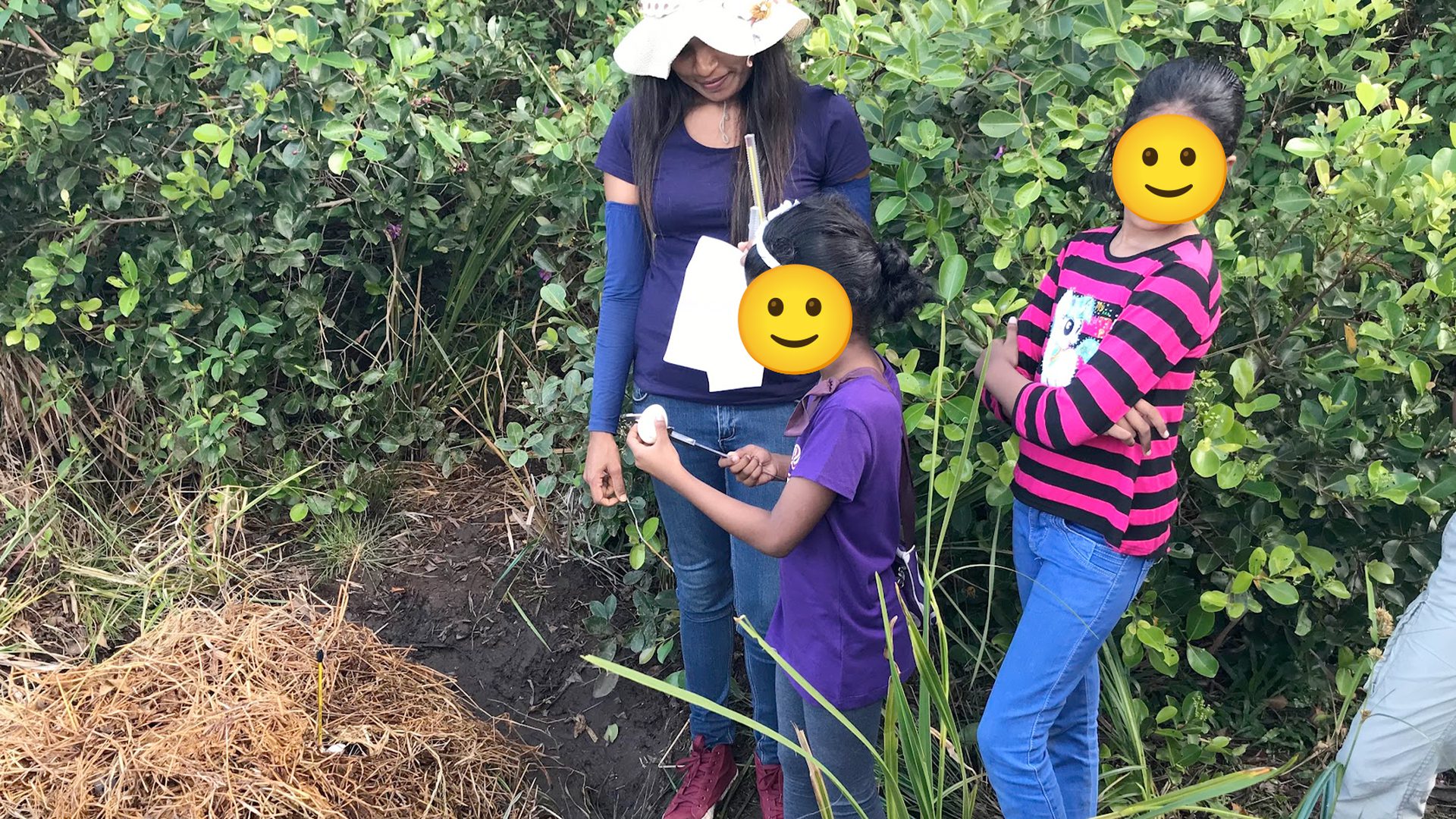 Children and an adult standing beside a mound of dry wetland vegetation during an outdoor demonstration